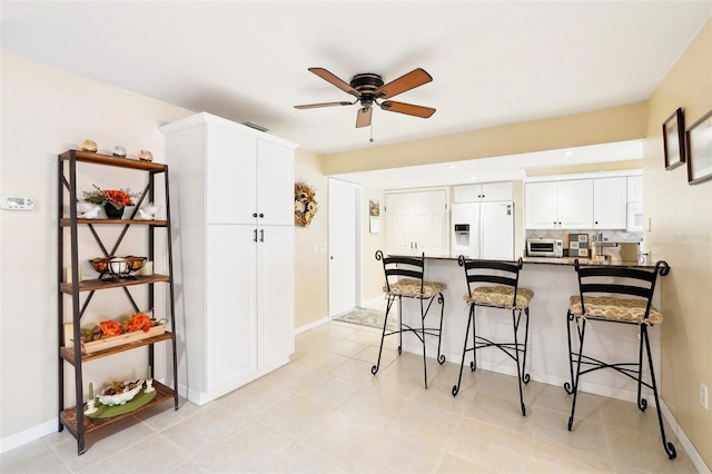 kitchen featuring a ceiling fan, a peninsula, white refrigerator with ice dispenser, white cabinetry, and a kitchen breakfast bar