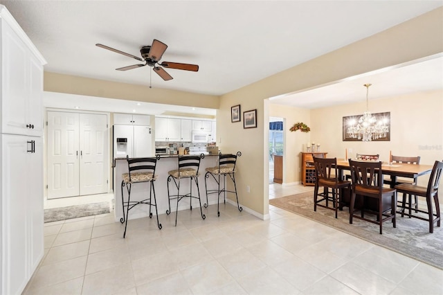 kitchen featuring ceiling fan with notable chandelier, dark countertops, white appliances, a breakfast bar area, and white cabinets