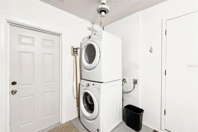 laundry area with a textured ceiling, stacked washer and clothes dryer, and laundry area