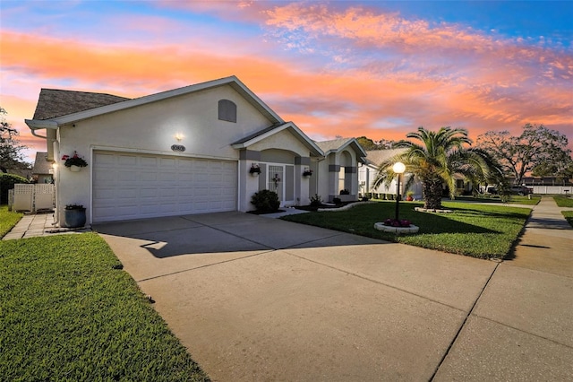 ranch-style home featuring stucco siding, a lawn, fence, concrete driveway, and an attached garage