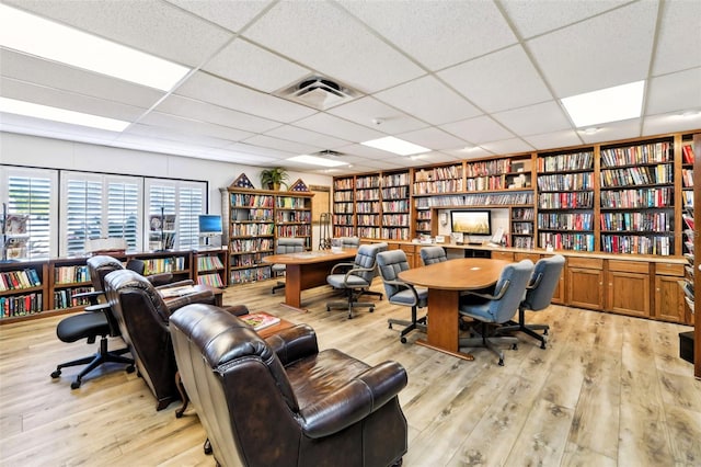 office space with light wood-style floors, wall of books, visible vents, and a drop ceiling