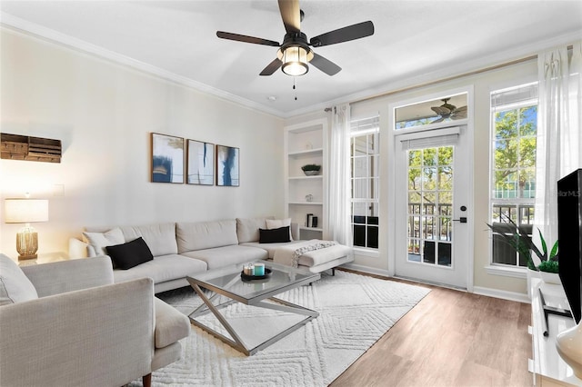 living room with ceiling fan, built in shelves, wood finished floors, and crown molding