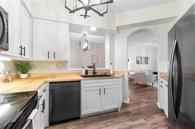 kitchen with wooden counters, dishwasher, freestanding refrigerator, arched walkways, and a sink