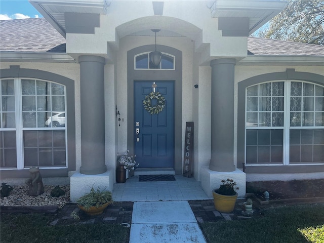 view of exterior entry with roof with shingles and stucco siding