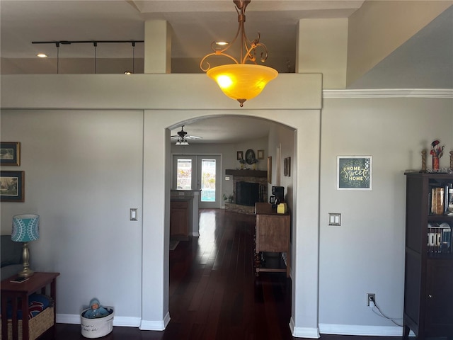 corridor with arched walkways, dark wood-style floors, and baseboards