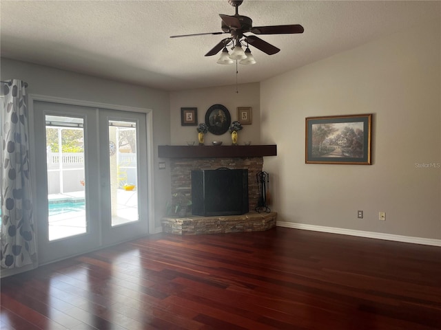 unfurnished living room with a stone fireplace, a textured ceiling, baseboards, and wood finished floors