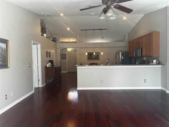 kitchen with dark wood-type flooring, stainless steel microwave, freestanding refrigerator, a peninsula, and brown cabinetry