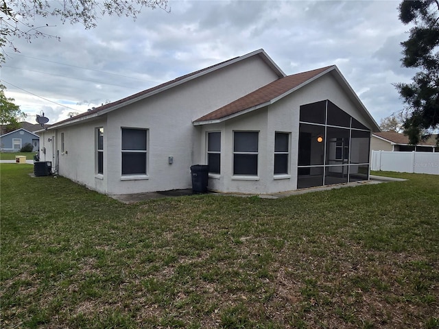 rear view of house with central air condition unit, a lawn, fence, and a sunroom