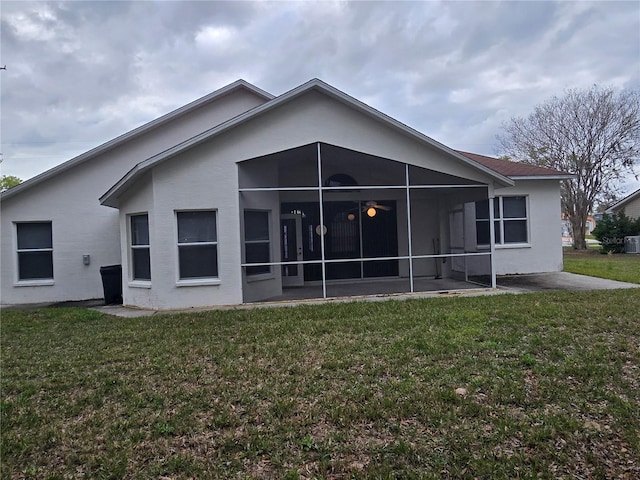 rear view of property with stucco siding, a yard, and a sunroom