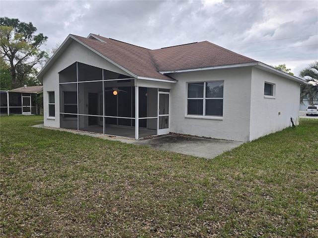 rear view of property with roof with shingles, stucco siding, a yard, a sunroom, and a patio area