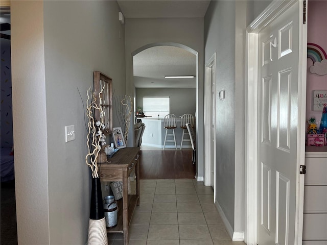 hallway with arched walkways, light tile patterned floors, and baseboards