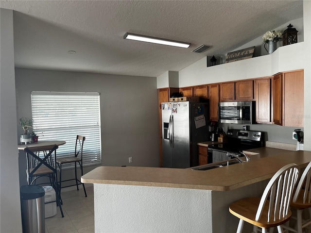 kitchen featuring visible vents, lofted ceiling, appliances with stainless steel finishes, brown cabinetry, and a sink