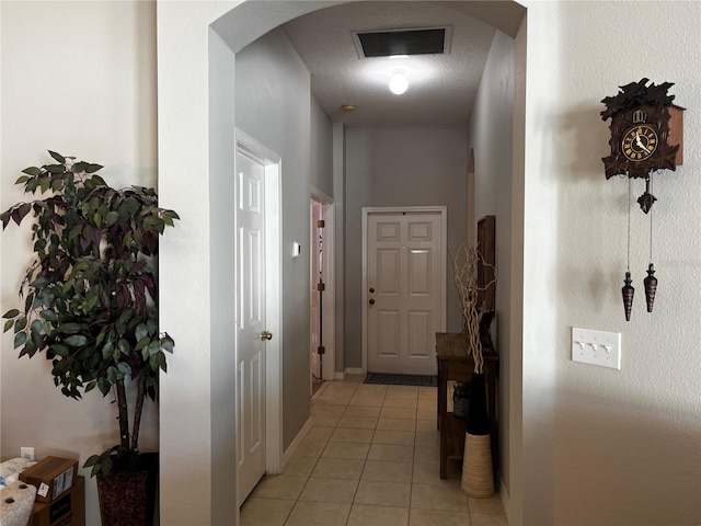 corridor with visible vents, baseboards, light tile patterned flooring, arched walkways, and a textured ceiling