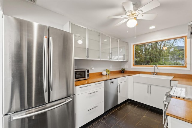 kitchen with ceiling fan, a sink, glass insert cabinets, appliances with stainless steel finishes, and white cabinetry