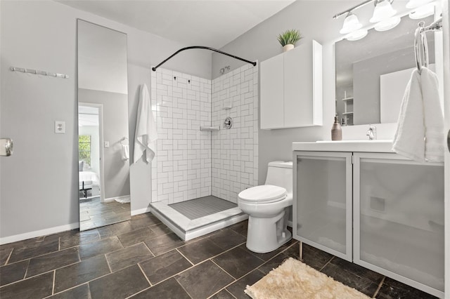 bathroom featuring stone finish flooring, baseboards, toilet, a tile shower, and vanity