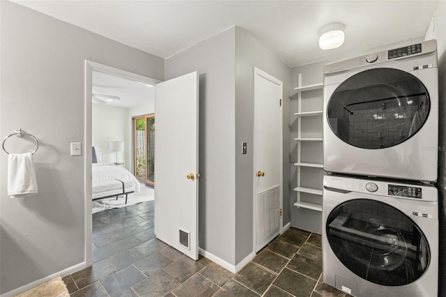 washroom featuring stone tile floors, visible vents, baseboards, laundry area, and stacked washer and clothes dryer