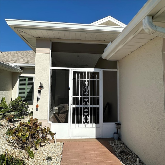 entrance to property featuring stucco siding and a shingled roof