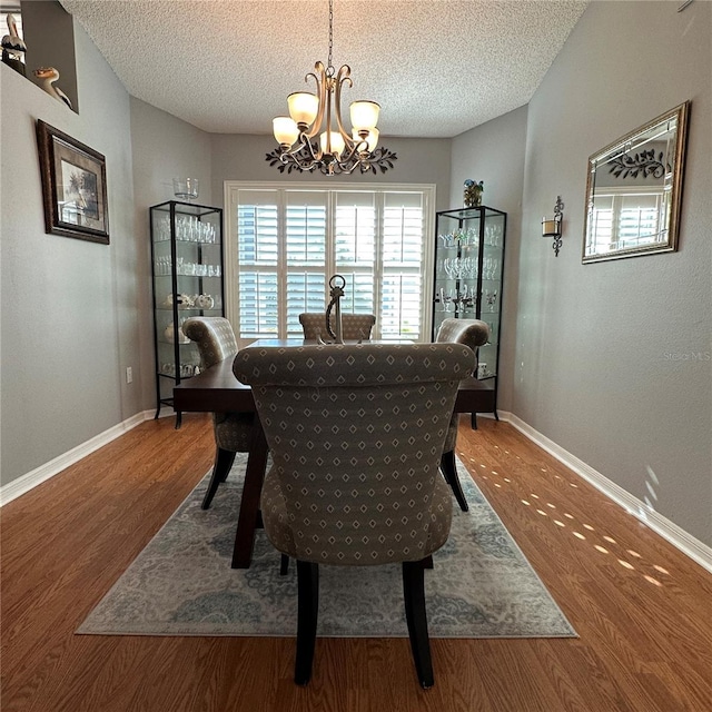 dining room featuring a textured ceiling, wood finished floors, baseboards, and a chandelier