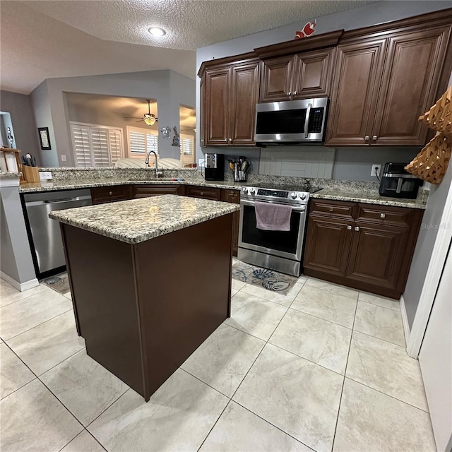 kitchen featuring dark brown cabinets, light stone countertops, lofted ceiling, a peninsula, and stainless steel appliances