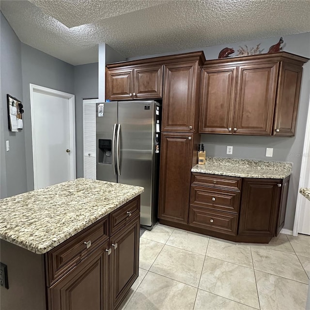 kitchen featuring light tile patterned floors, stainless steel fridge, a textured ceiling, and light stone countertops