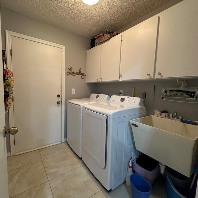 clothes washing area with washer and dryer, a sink, a textured ceiling, cabinet space, and light tile patterned floors