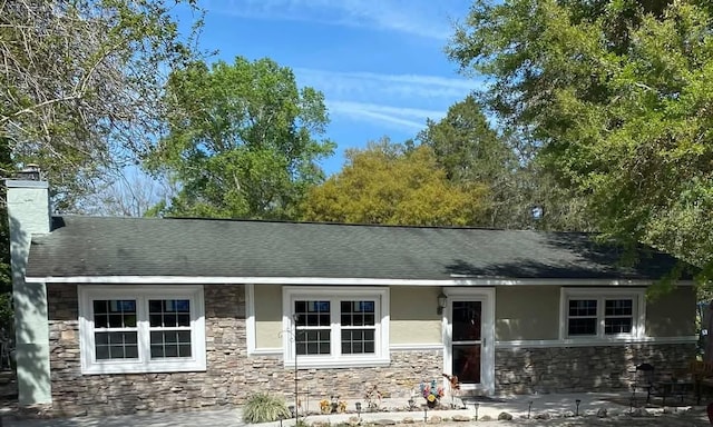 ranch-style home with stucco siding, stone siding, roof with shingles, and a chimney