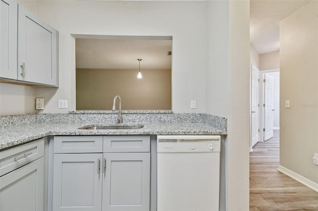 kitchen with a sink, light stone counters, light wood-style floors, white dishwasher, and baseboards