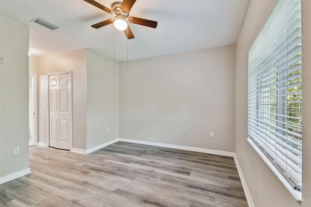 spare room with a ceiling fan, wood finished floors, visible vents, and baseboards