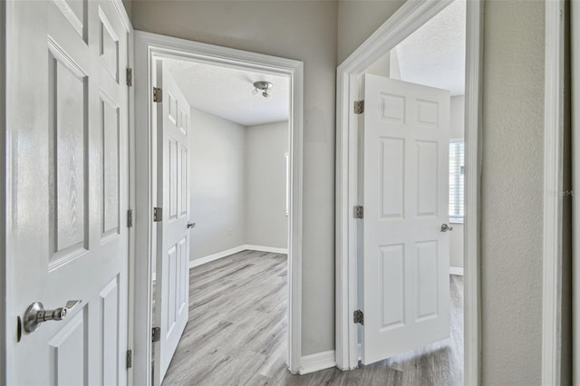 corridor with light wood-style flooring, baseboards, and a textured ceiling