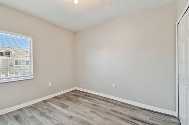 unfurnished room featuring light wood-type flooring, baseboards, and a textured ceiling