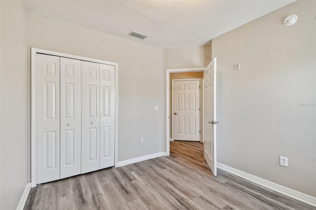 unfurnished bedroom with baseboards, visible vents, light wood-style floors, a closet, and a textured ceiling