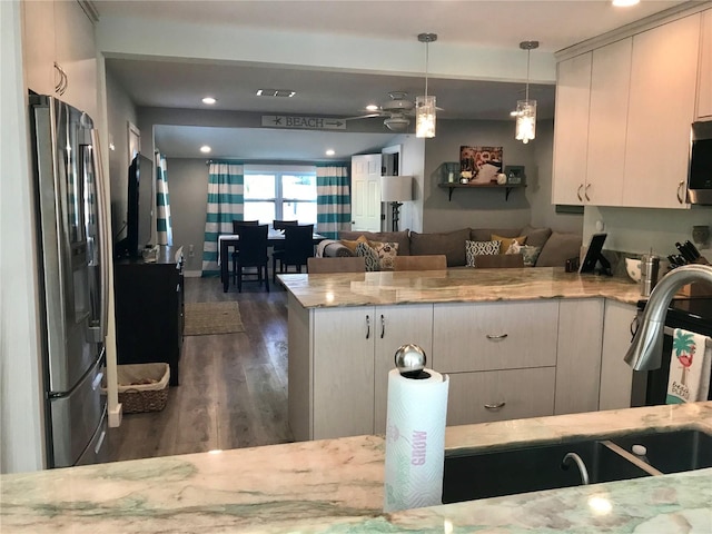 kitchen featuring open floor plan, pendant lighting, light stone counters, a peninsula, and stainless steel appliances