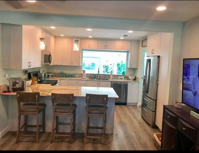 kitchen featuring light wood-type flooring, a sink, appliances with stainless steel finishes, a peninsula, and light countertops