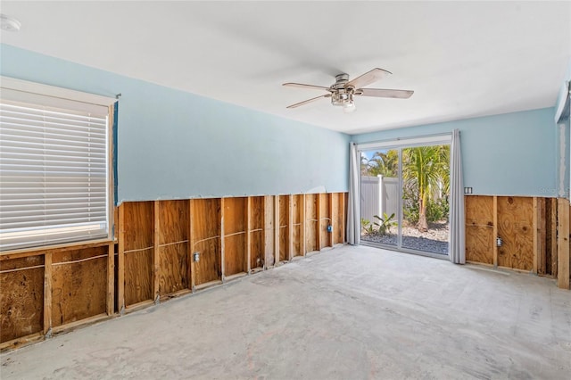 unfurnished room with unfinished concrete floors, a ceiling fan, wood walls, and wainscoting