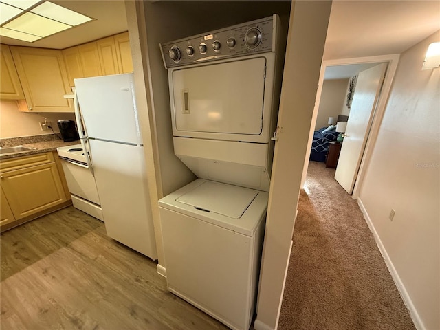 laundry area with baseboards, light wood-type flooring, light carpet, laundry area, and stacked washer / drying machine