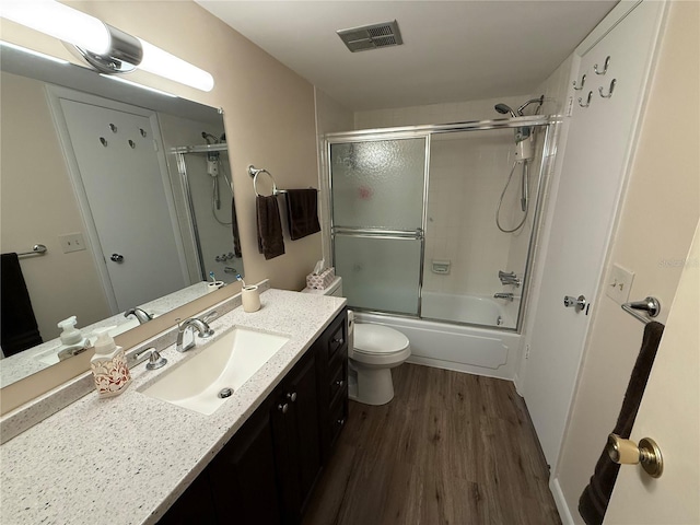 full bathroom featuring vanity, wood finished floors, visible vents, toilet, and combined bath / shower with glass door