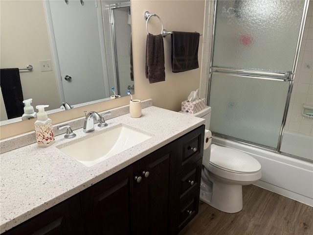 bathroom with vanity, toilet, wood finished floors, and shower / bath combination with glass door