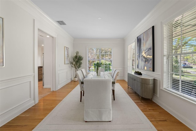 dining area with visible vents, a decorative wall, crown molding, and light wood finished floors