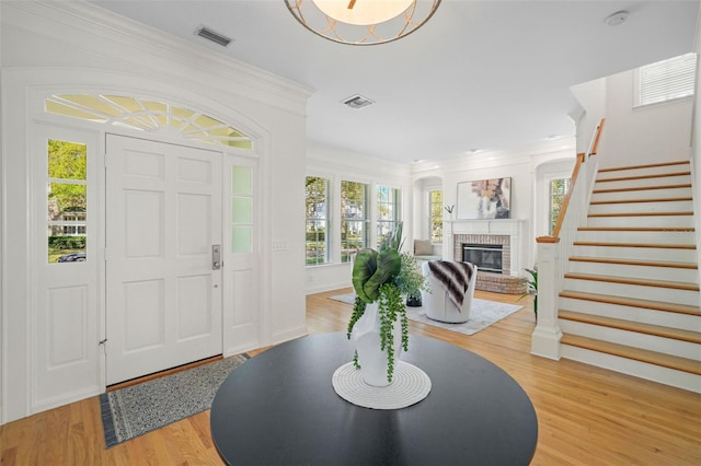 entryway with visible vents, stairway, light wood-type flooring, and a brick fireplace