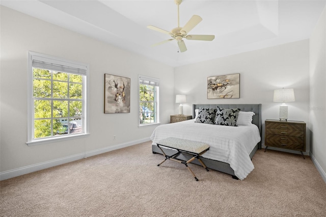 carpeted bedroom with a tray ceiling, baseboards, and a ceiling fan