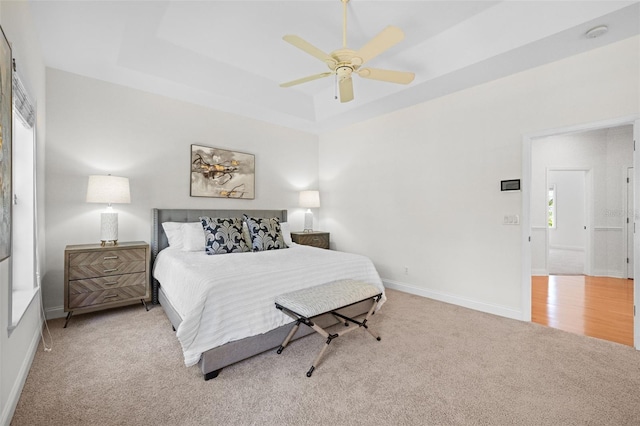 carpeted bedroom featuring ceiling fan, a raised ceiling, and baseboards