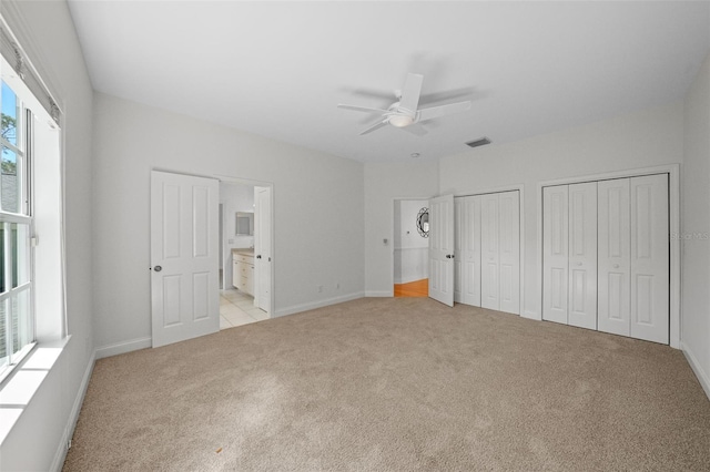 unfurnished bedroom with visible vents, baseboards, ensuite bath, light colored carpet, and two closets