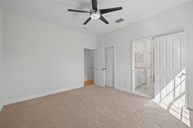 unfurnished bedroom with visible vents, baseboards, light colored carpet, ensuite bath, and a ceiling fan