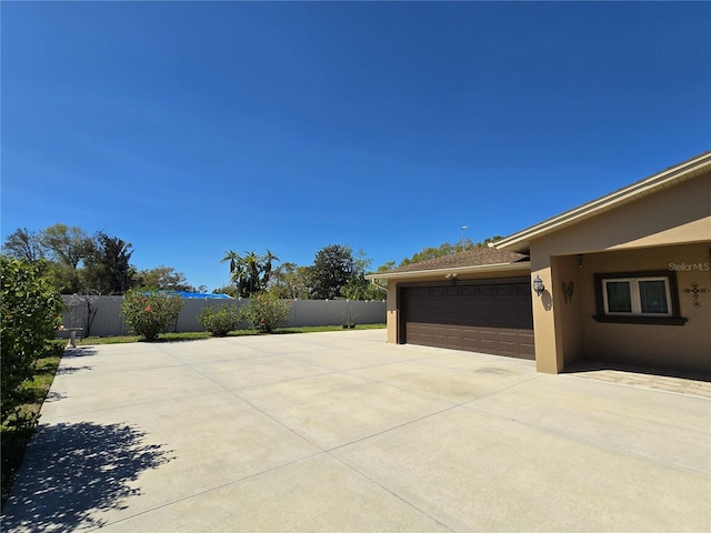 view of property exterior with stucco siding, a garage, driveway, and fence