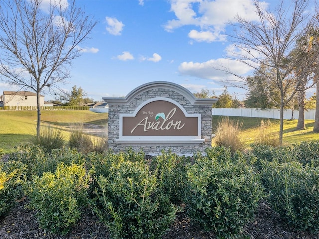 community / neighborhood sign featuring fence and a lawn