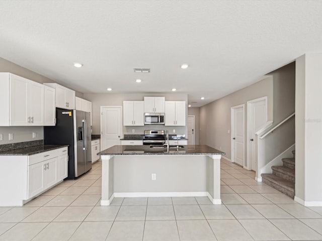 kitchen featuring light tile patterned floors, appliances with stainless steel finishes, white cabinetry, and dark stone counters