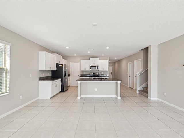 kitchen featuring dark countertops, baseboards, light tile patterned floors, appliances with stainless steel finishes, and white cabinets