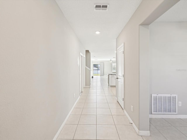 corridor featuring light tile patterned floors, visible vents, and baseboards