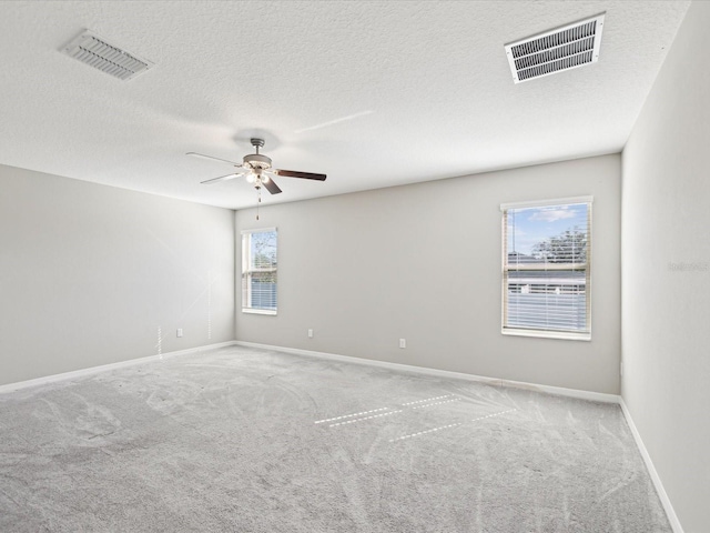 carpeted empty room with visible vents, a textured ceiling, baseboards, and ceiling fan