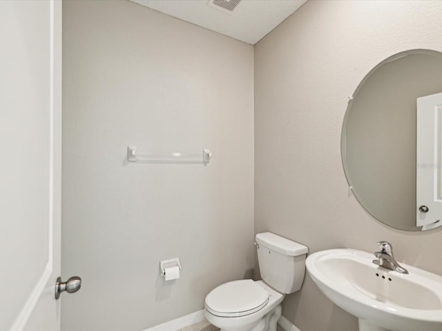 half bathroom with a sink, visible vents, baseboards, and toilet